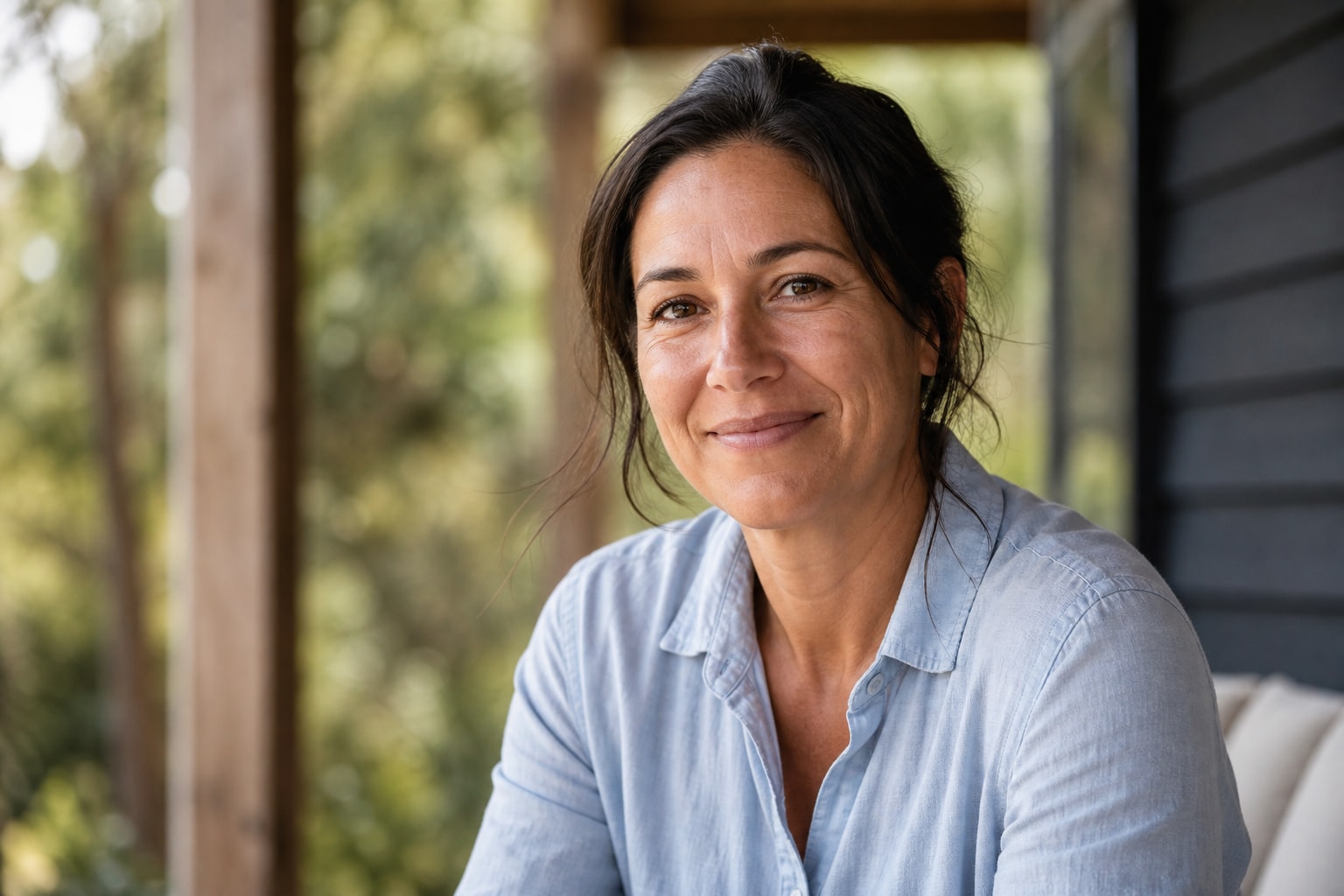 Illustrative portrait: a woman with a relaxed smile on a shaded veranda.