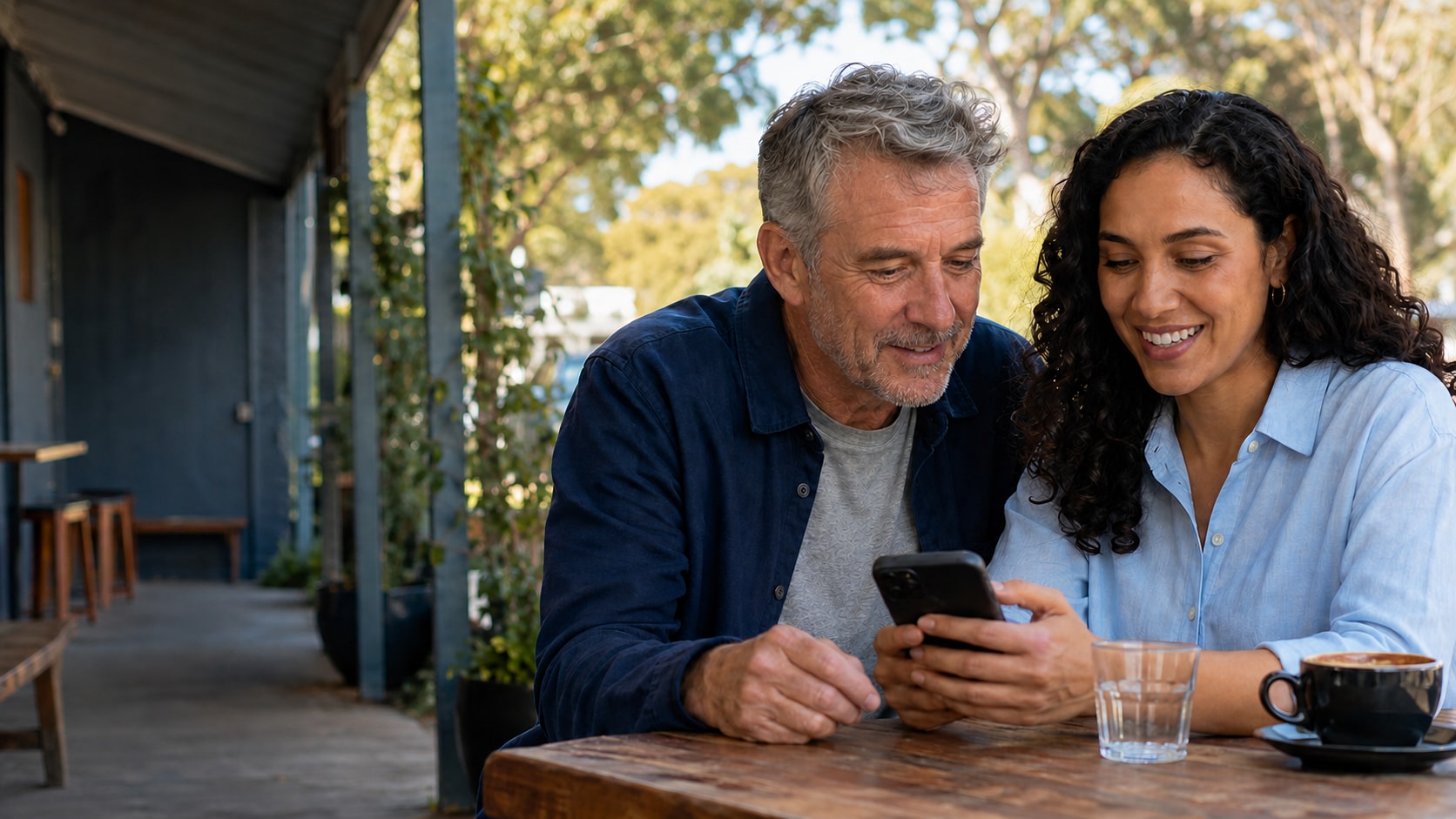 Illustrative scene: two adults looking at a phone together at an Australian café.